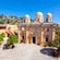 The stone façade of the Agia Triada Monastery reveals classic Greek architecture with columns, a pediment and 3 domes